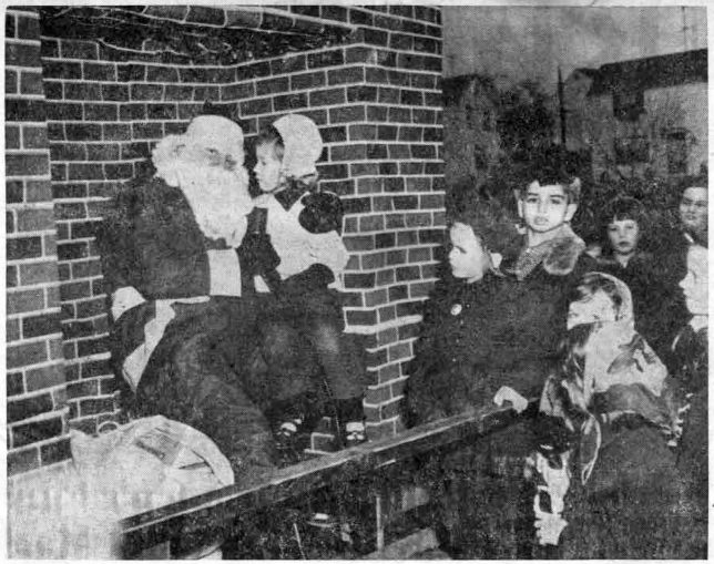 Little Susan Jones makes sure that Santa Claus (William Fanus) knows what she wants for Christmas, as she sits under the fireplace with Old St. Nick while other children from the Wayne Terraces area look on. The photo was taken just after Santa’s unusual arrival on the Radnor Fire Company ladder truck on Saturday. (Photo by Stellabott Studio)